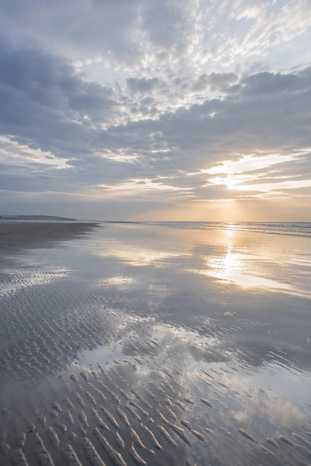 Open tidal flat on the North Somerset coast — calm water, wide sky, light breaking through
